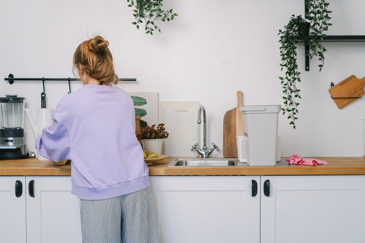 expertise-01 Back view of unrecognizable young female in casual clothes standing at wooden counter in light kitchen in daytime